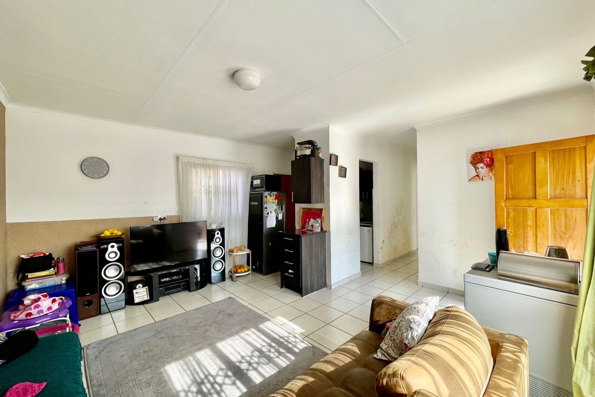 A living area featuring tiled flooring and access to a hallway, showing signs of wear on the walls.