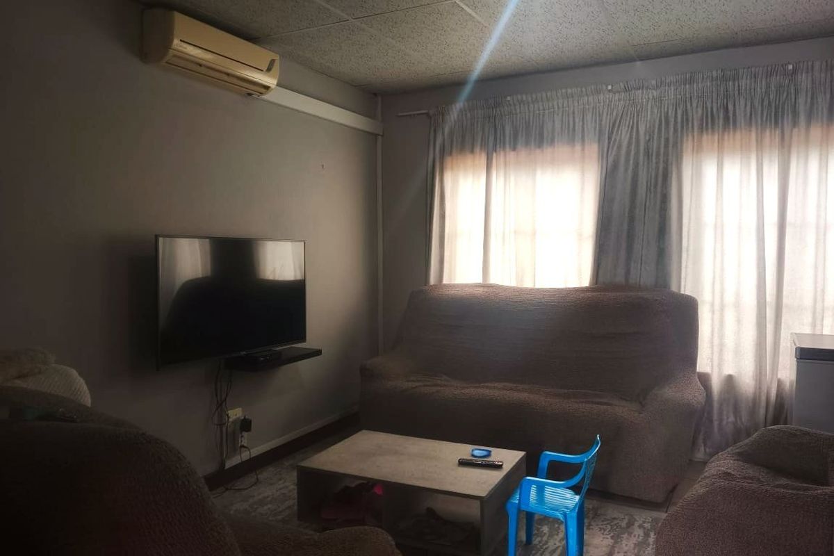 A living room featuring a wall-mounted air conditioning unit and large windows with curtains, providing a functional space for relaxation.