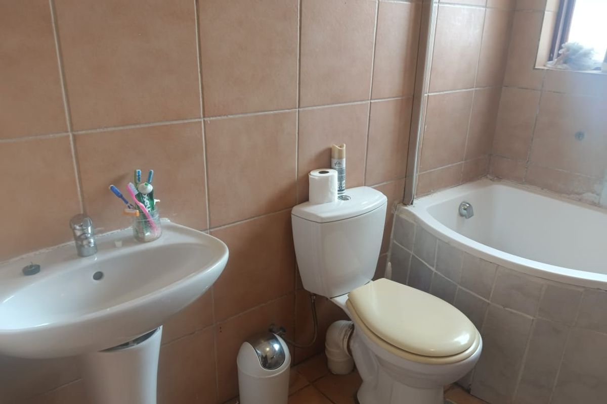 A functional bathroom featuring a pedestal basin, toilet, and bathtub with dated wall and floor tiling, offering potential for modernization.