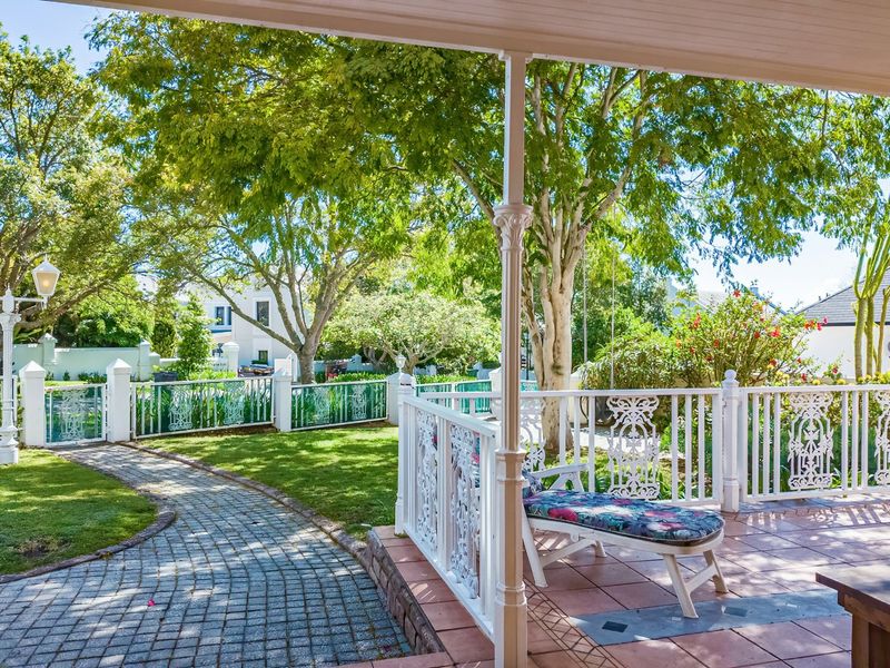A covered patio featuring decorative wrought iron balustrades and tiled flooring, overlooking a well-maintained garden with a cobblestone pathway.
