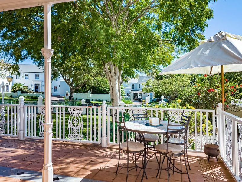 A covered patio featuring tiled flooring and decorative metal balustrades, overlooking a lush garden area with mature trees.