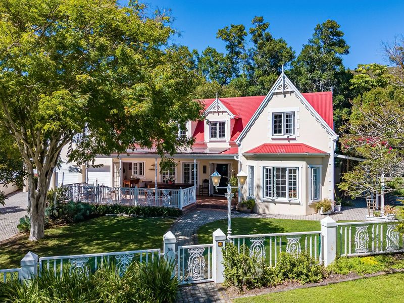 Charming double-story residence featuring a distinctive red corrugated metal roof, dormer windows, and a welcoming covered patio set within a landscaped garden.