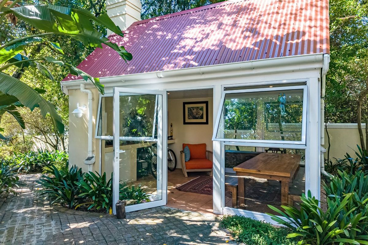A charming garden outbuilding featuring a red corrugated roof, large aluminium windows, and french doors opening onto a brick-paved patio area.