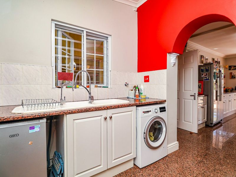 A functional laundry area featuring granite countertops, a double basin sink, built-in cabinetry, and tiled flooring, connected to the main living space via an archway.