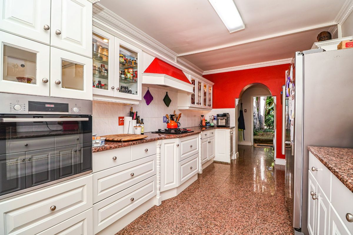 A functional kitchen featuring white shaker-style cabinetry, granite countertops, built-in oven, gas hob, and polished granite flooring, leading through an archway to the rear.