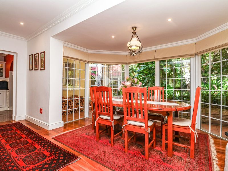 A bright dining room featuring hardwood flooring, crown molding, and a large bay window with views of the garden.