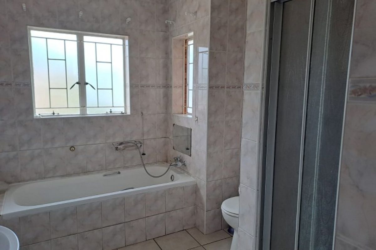 A functional bathroom featuring a built-in bathtub, separate shower enclosure, toilet, and neutral wall and floor tiling throughout.