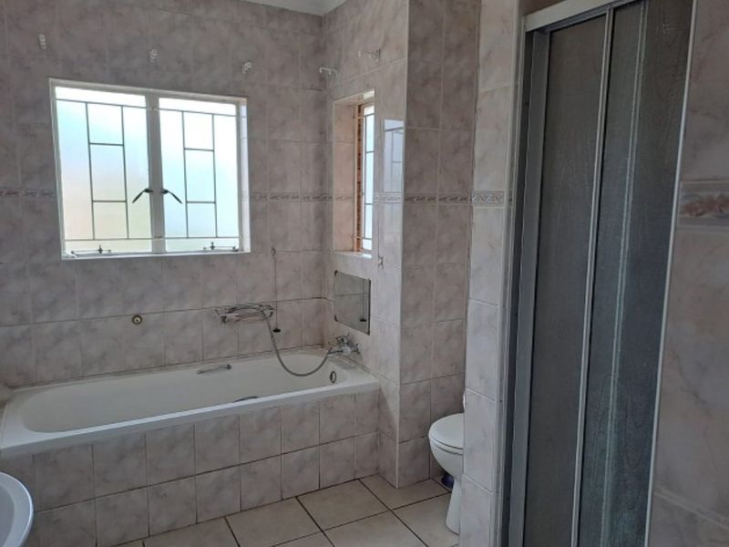A functional bathroom featuring a built-in bathtub, separate shower enclosure, toilet, and neutral wall and floor tiling throughout.
