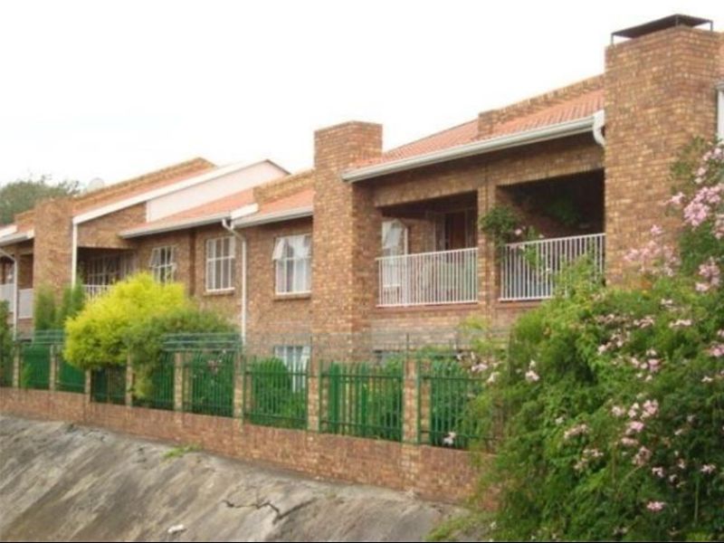 A multi-unit apartment complex featuring face brick construction, tiled roofing, and secure metal perimeter fencing with balcony access.