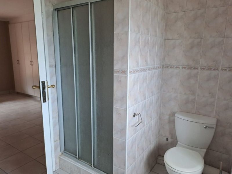 A functional bathroom featuring a shower enclosure, toilet, and neutral wall tiling, with adjacent built-in storage cupboards visible in the background.