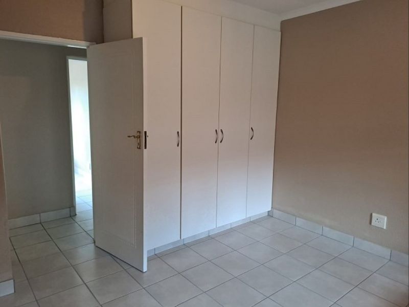 A clean, empty bedroom featuring neutral tiled flooring and white built-in cupboards, offering a versatile space ready for personalization.