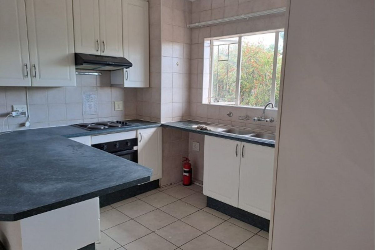 A functional kitchen featuring white cabinetry, dark laminate countertops, a built-in oven and hob, and a double basin sink with tiled splashbacks.