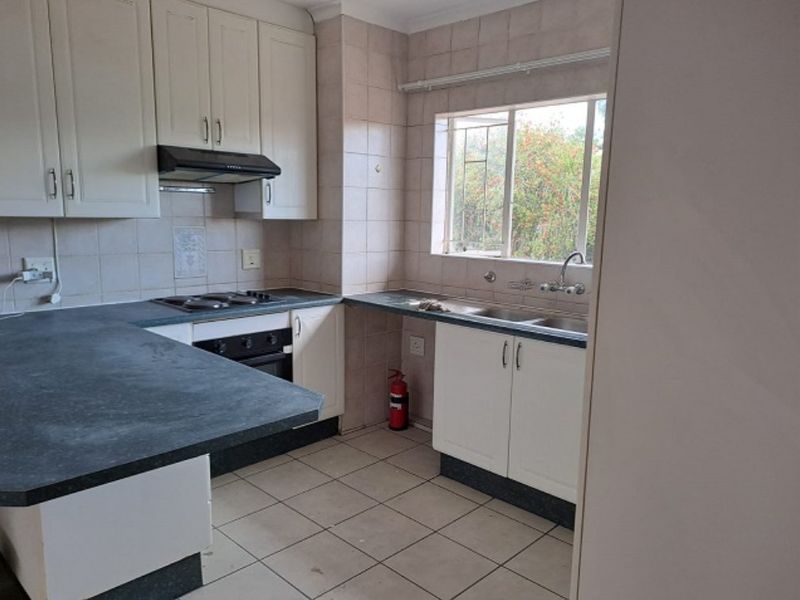 A functional kitchen featuring white cabinetry, dark laminate countertops, a built-in oven and hob, and a double basin sink with tiled splashbacks.