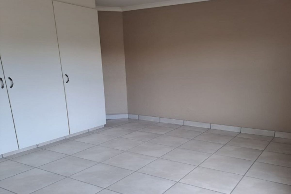An empty bedroom featuring neutral wall paint, tiled flooring, and built-in cupboards.