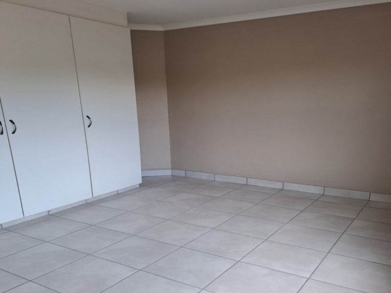 An empty bedroom featuring neutral wall paint, tiled flooring, and built-in cupboards.