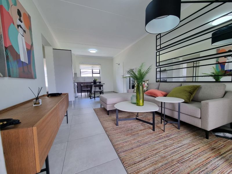 An open-plan living and kitchen area featuring modern tiled flooring, neutral walls, and integrated kitchen cabinetry, creating a bright and functional living space.