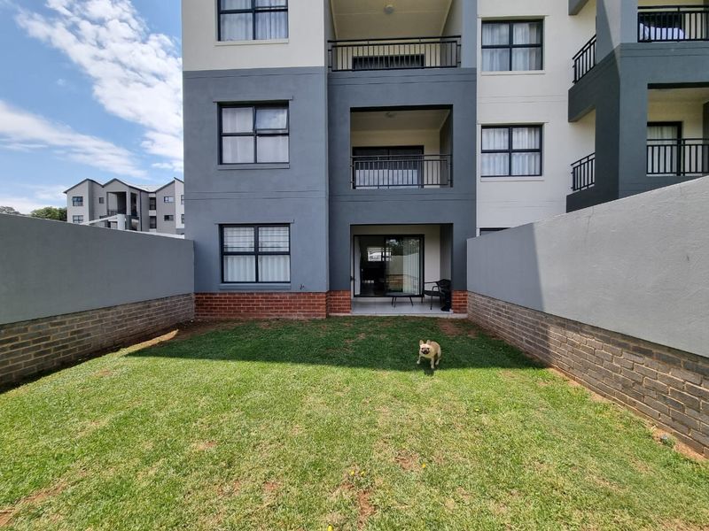 A private rear garden featuring a lawn and brick boundary walls, with direct access to the townhouse via a covered patio and sliding glass door.