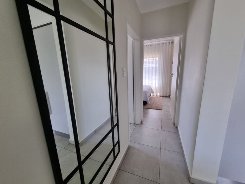 A clean and bright hallway featuring neutral tiled flooring and white walls, providing access to adjacent rooms.