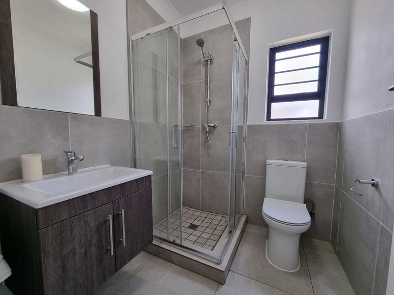 A modern, well-maintained bathroom featuring a vanity cabinet, a glass-enclosed shower, and neutral wall and floor tiling.