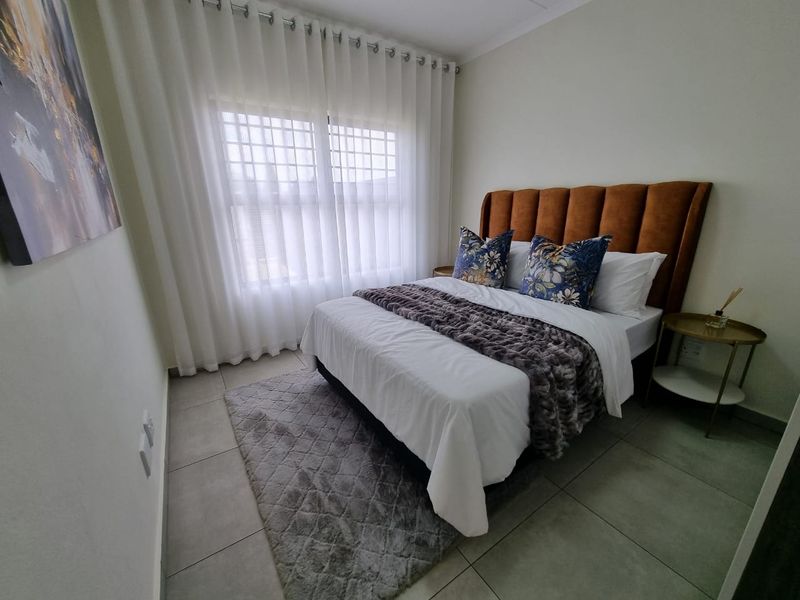 A well-maintained bedroom featuring neutral tiled flooring and a window fitted with security bars, offering a clean and functional living space.