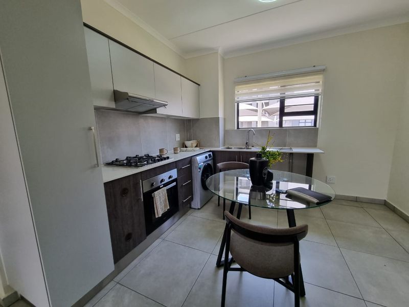 Modern kitchen featuring dark and light cabinetry, stone countertops, gas hob, built-in oven, extractor fan, and tiled flooring with an integrated laundry connection.