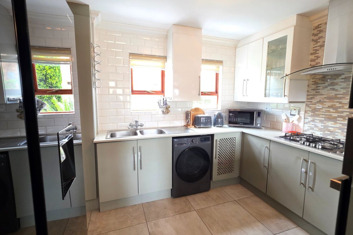 A functional kitchen featuring light-toned cabinetry, subway tile backsplash, a double basin sink, gas hob with extractor, and tiled flooring.