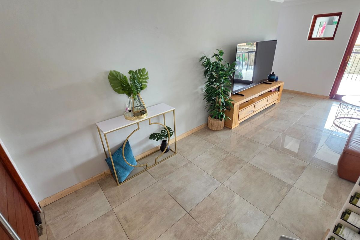 A bright living area featuring large format floor tiles, neutral wall finishes, and direct access to an outdoor balcony through a glass door.