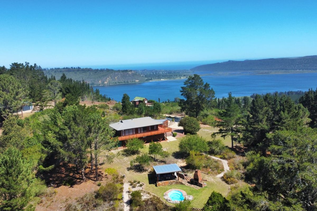 Aerial view of a farm property featuring a main residence with a wooden deck, a swimming pool, and an outdoor fireplace set in a landscape.
