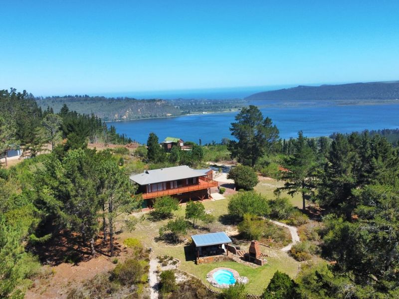 Aerial view of a farm property featuring a main residence with a wooden deck, a swimming pool, and an outdoor fireplace set in a landscape.