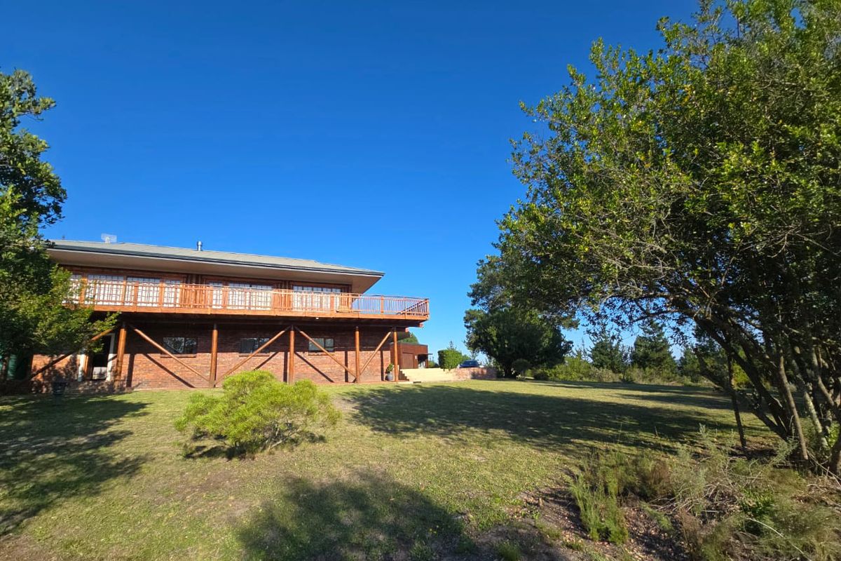 Rear view of the farm property featuring a large raised wooden deck, brick exterior walls, and expansive surrounding garden grounds.