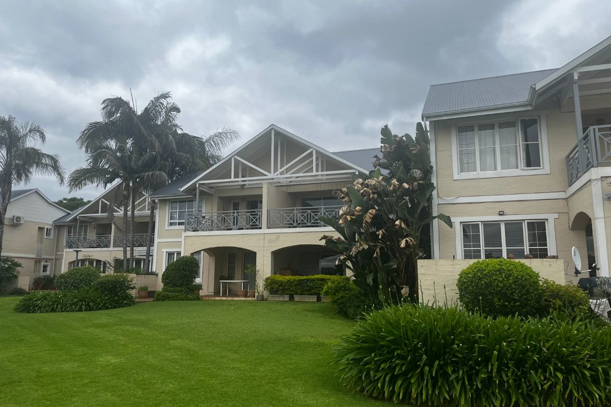 Rear view of the apartment complex featuring a well-maintained lawn, landscaped garden, and covered patio areas with balcony access.