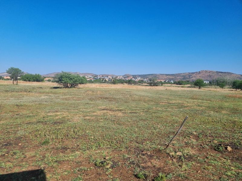 A wide-angle view of a vacant residential plot featuring natural grass and shrubs with distant mountain and neighborhood views.