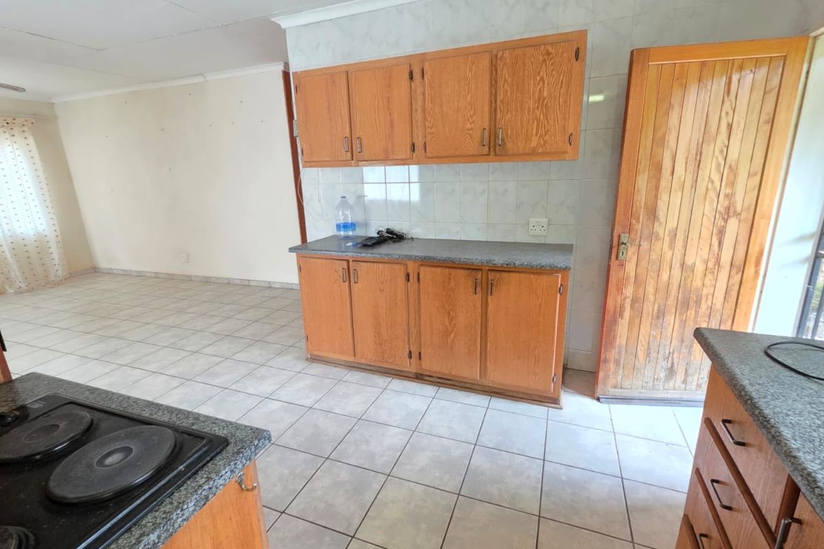 An open-plan kitchen area featuring dated timber cabinetry, laminate countertops, and ceramic tiling, offering a blank canvas for potential modern renovation.