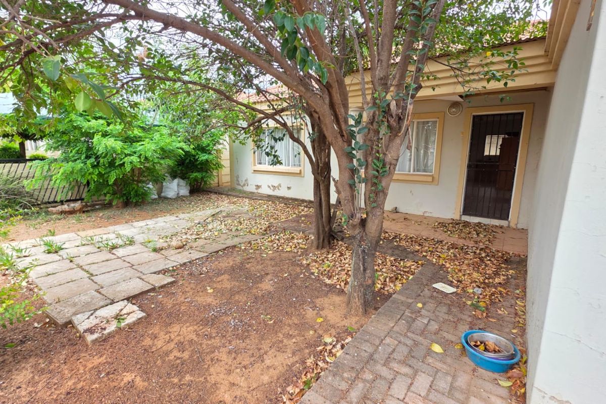 Rear exterior view of the property featuring a paved walkway, security gate, and garden area requiring maintenance and cosmetic attention.