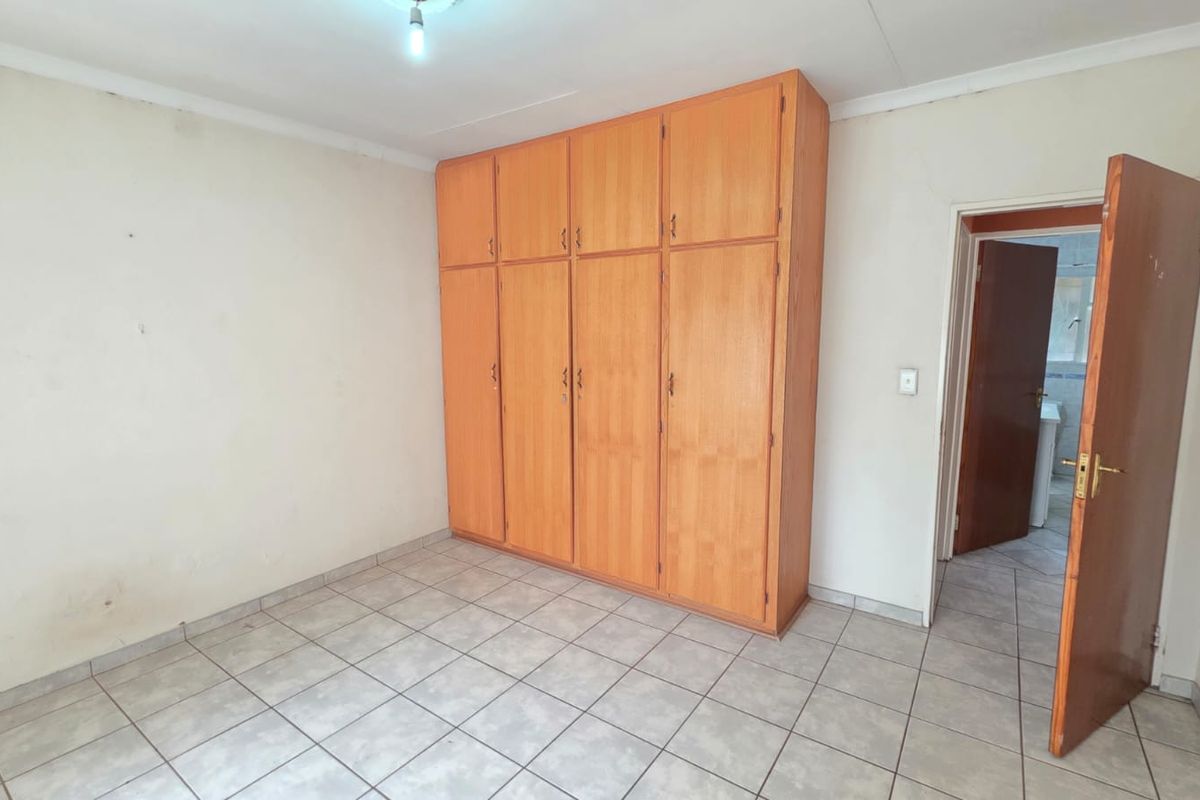 An empty bedroom featuring tiled flooring and built-in wooden cupboards, offering a blank canvas for personalization.