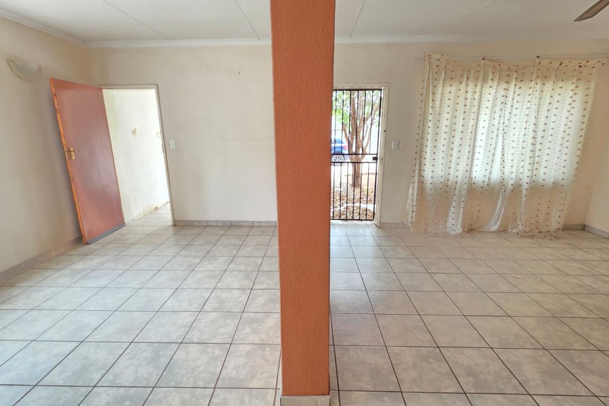 An open-plan living area featuring ceramic floor tiles, a central structural pillar, and direct access to the exterior via a security gate.