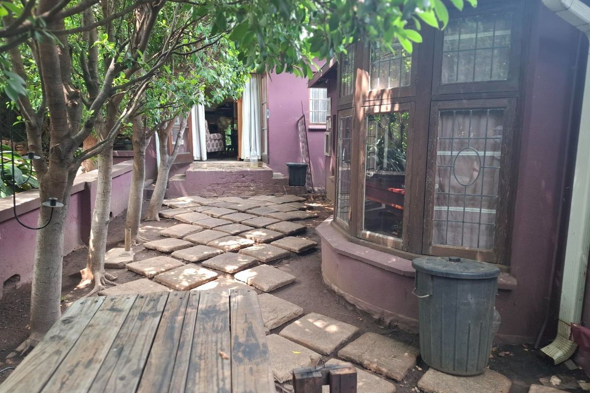 Rear garden area featuring a stone paver pathway, mature trees, and a bay window overlooking the outdoor space.