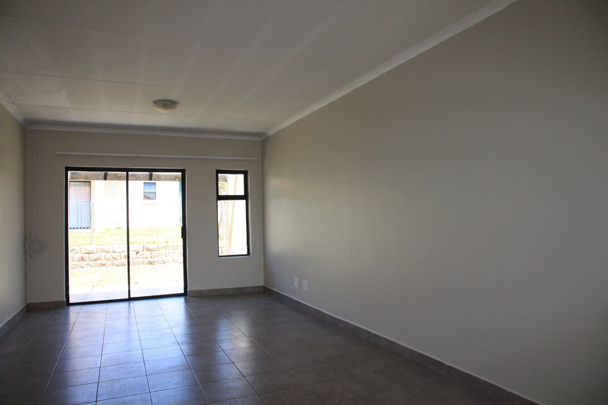 A bright, empty living room featuring neutral walls, tiled flooring, and a sliding glass door providing access to the exterior.