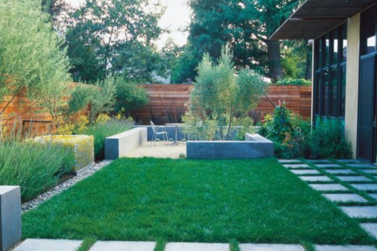 A well-maintained rear garden featuring a manicured lawn, concrete paver pathways, raised concrete planter beds, and timber boundary fencing.