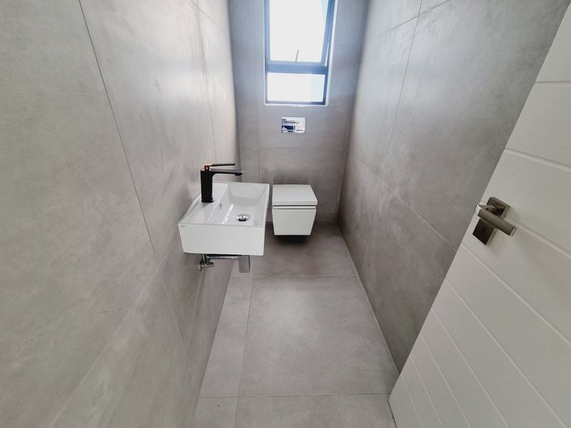 A modern, minimalist guest bathroom featuring large format grey tiles, a wall-hung toilet with a concealed cistern, and a sleek wall-mounted basin.