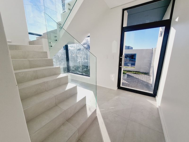 Modern entrance hall featuring a tiled staircase with a sleek glass balustrade, large glass door, and bright, open-plan architectural design.