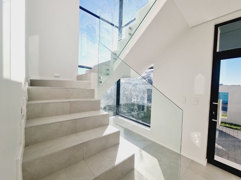Modern entrance hallway featuring a tiled staircase with a sleek glass balustrade and large windows providing ample natural light.