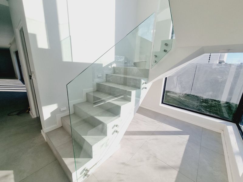 Modern staircase featuring tiled steps, a frameless glass balustrade, and a large window providing ample natural light in an open hallway space.