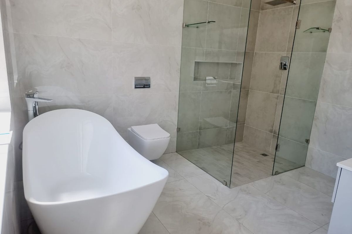 Modern bathroom featuring a sleek freestanding bathtub, a wall-mounted toilet, and a spacious walk-in glass shower with a recessed niche and marble-look tiling.