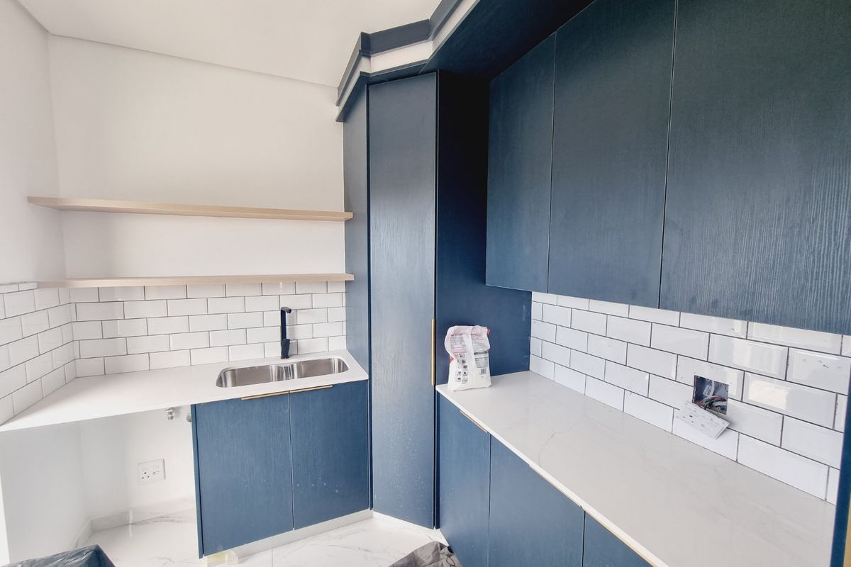 Modern kitchen featuring navy blue cabinetry, white stone countertops, subway tile backsplash, and floating shelves, currently awaiting final electrical finishing.