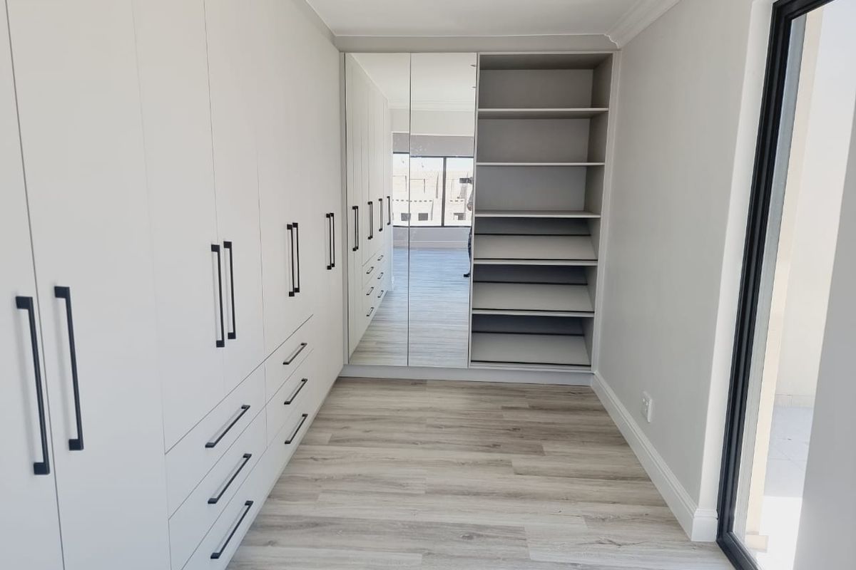 A modern, empty walk-in closet or dressing area featuring extensive built-in cabinetry, mirrored wardrobe doors, and light-toned laminate flooring.