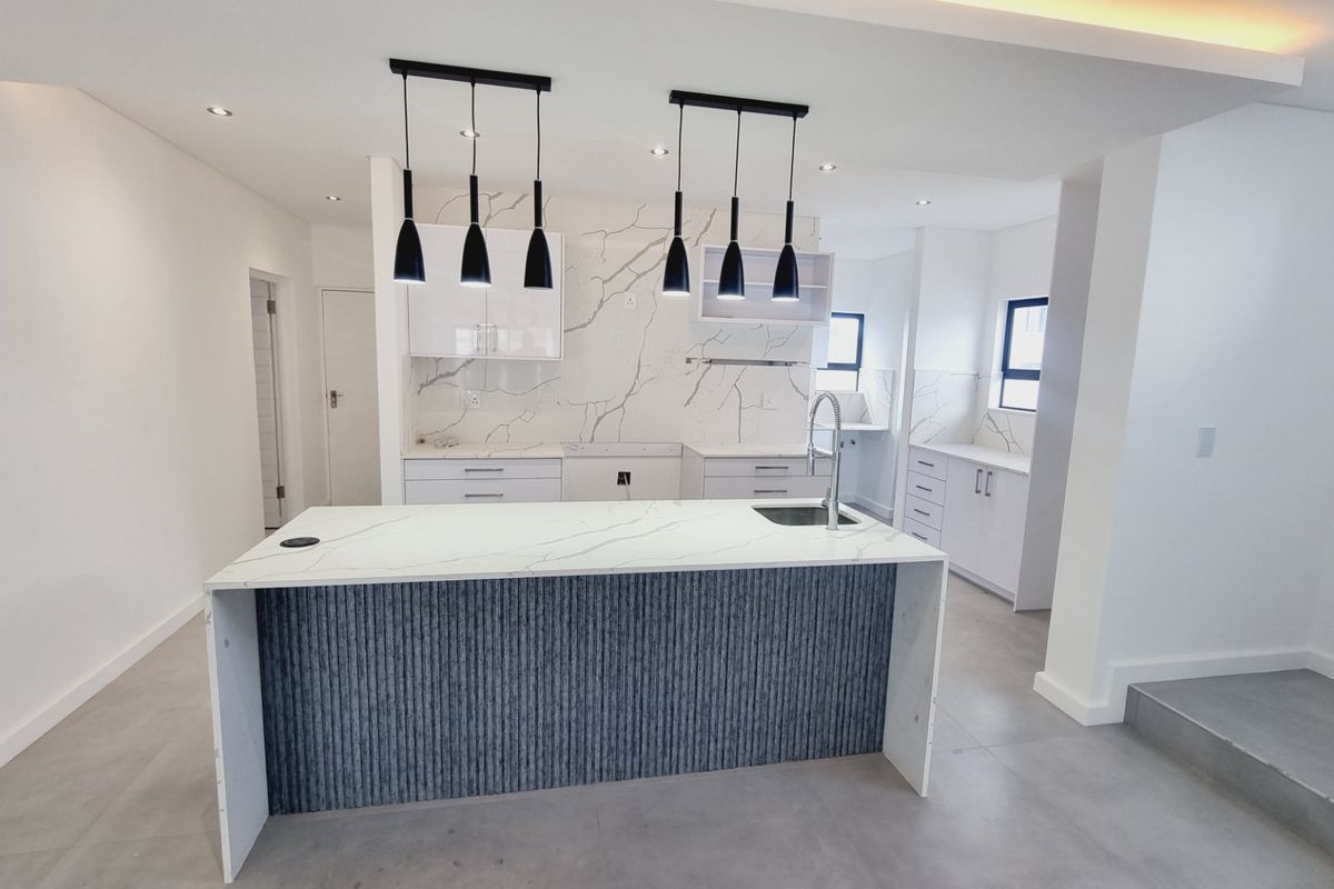 Modern, open-plan kitchen featuring a central island with stone countertops, marble-look splashbacks, sleek cabinetry, and contemporary pendant lighting.