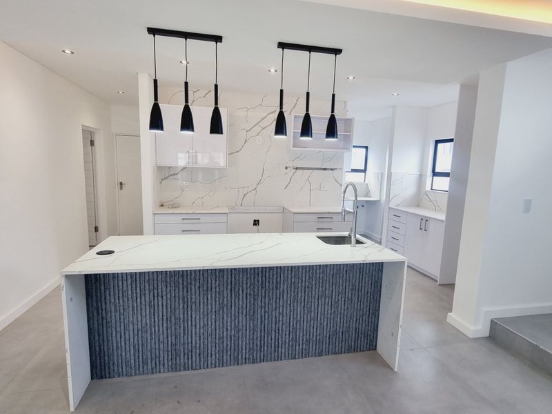 Modern, open-plan kitchen featuring a central island with stone countertops, marble-look splashbacks, sleek cabinetry, and contemporary pendant lighting.