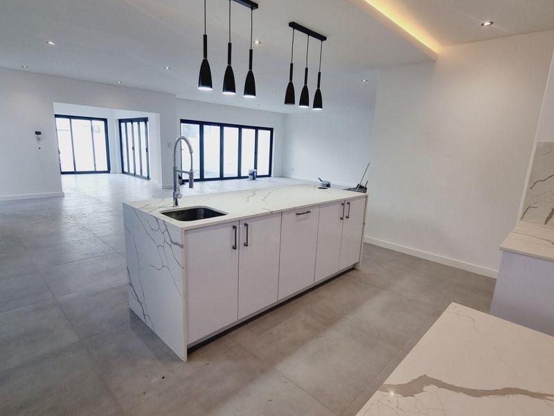 Spacious open-plan kitchen and living area featuring a modern island with marble-look quartz countertops, large format floor tiles, and expansive bi-fold doors.