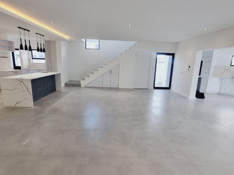 Spacious open-plan living area featuring a modern kitchen with stone island, sleek cabinetry, and tiled flooring, complemented by a staircase with integrated storage.